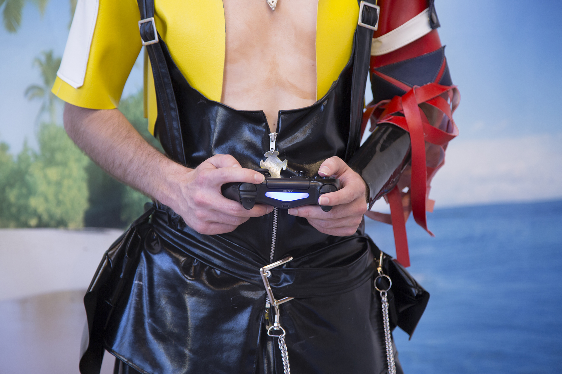Detail of Jesse's hands with a cnotroller while dressed in cosplay playing video games on an artificial beach set